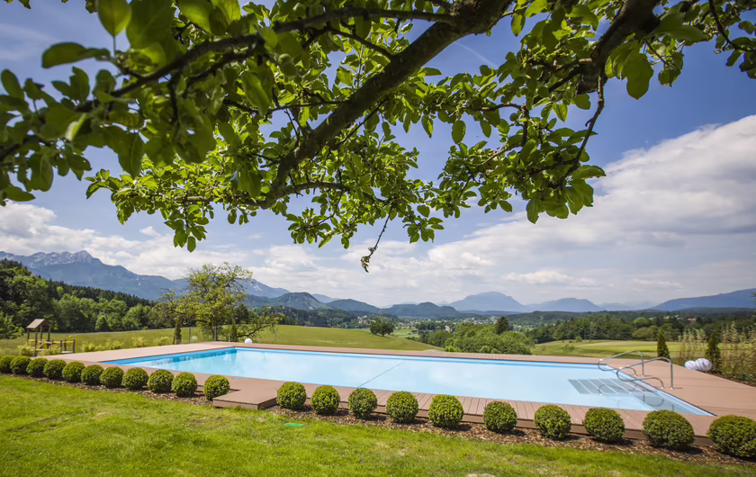 Outdoor Pool im Sommer mit grünen Bäumen und Ausblick auf die Berge