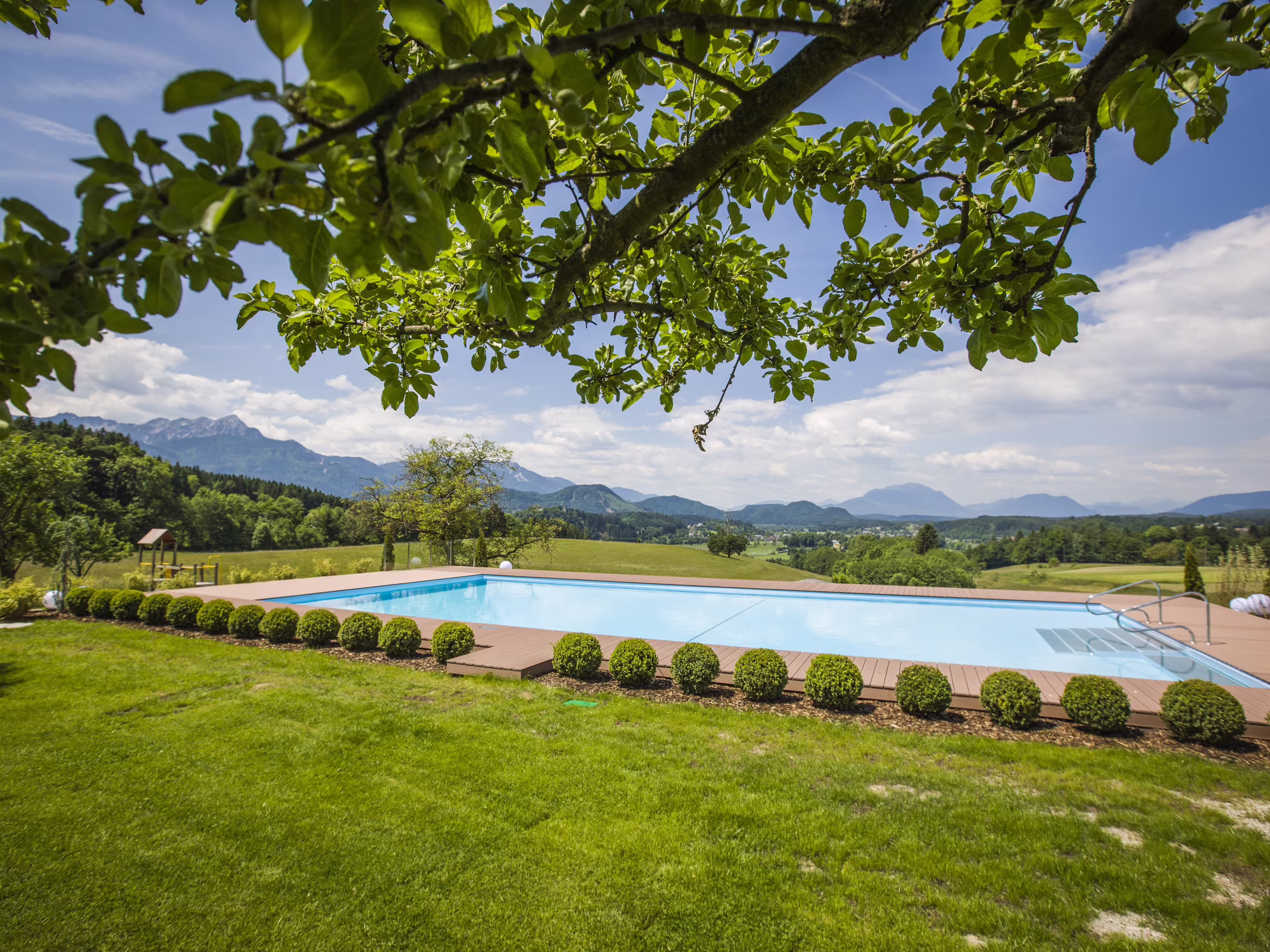 Outdoor Pool im Sommer mit grünen Bäumen und Ausblick auf die Berge