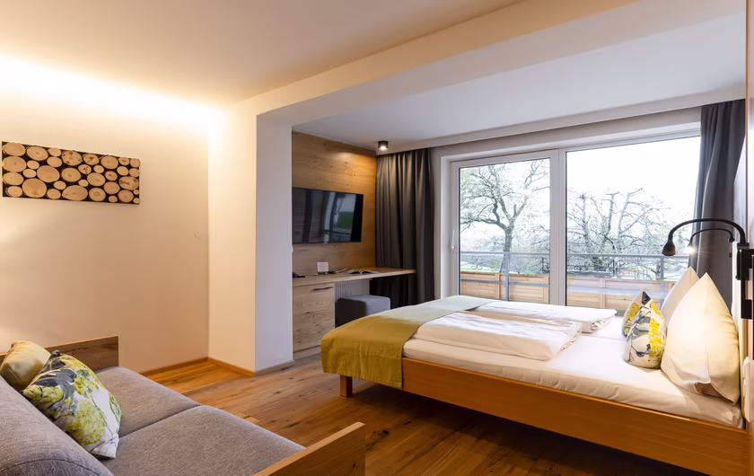 großes Zimmer mit Couch, Doppelbett, Schreibtisch und Fenster