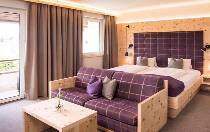 großes Zimmer mit Zirbenholz, Fenster, lila kariertem Couch- und Kopfbezug