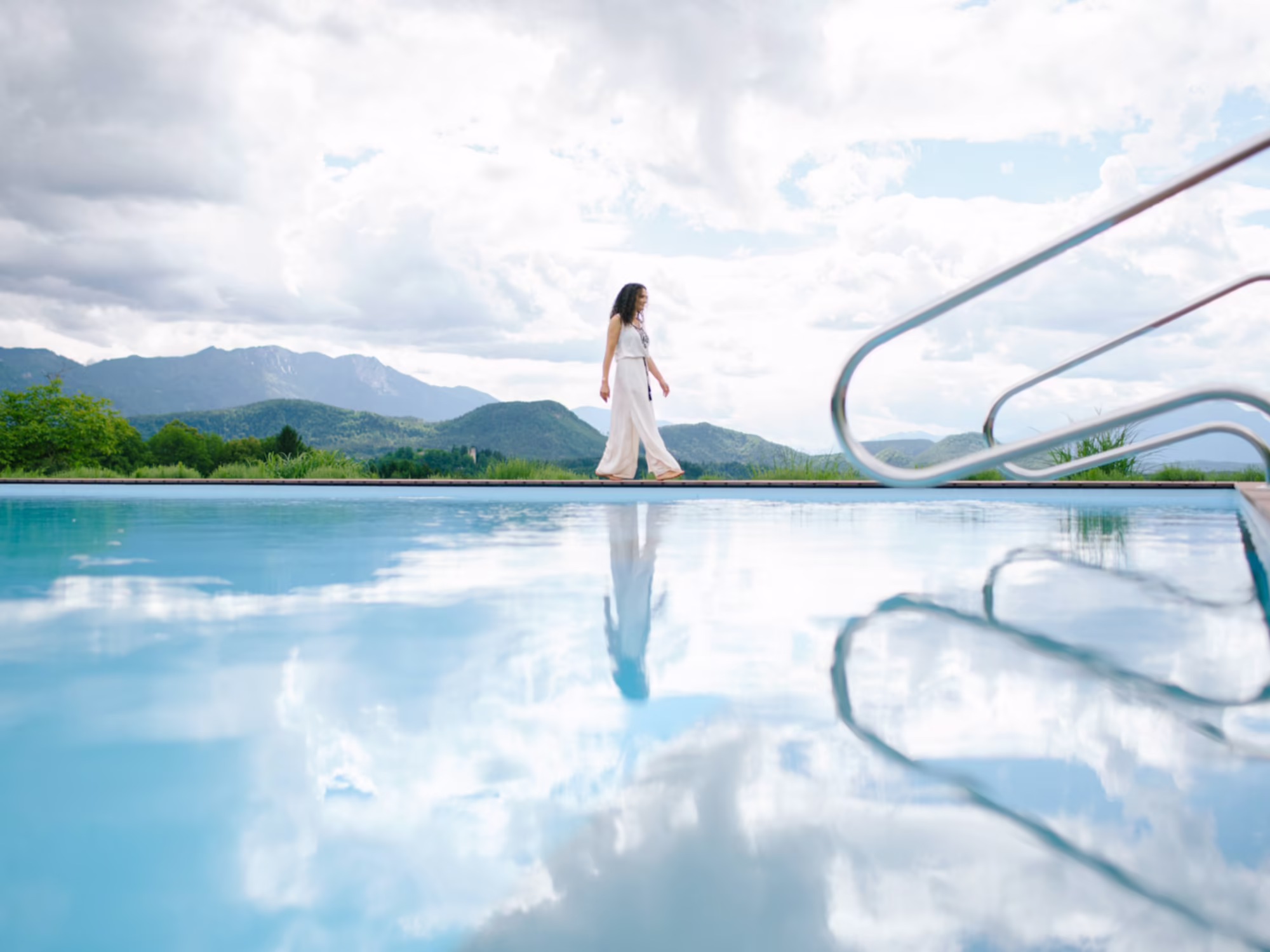 weiß gekleidete Frau geht am Outdoor Pool Rand bei bewöltkem Wetter 