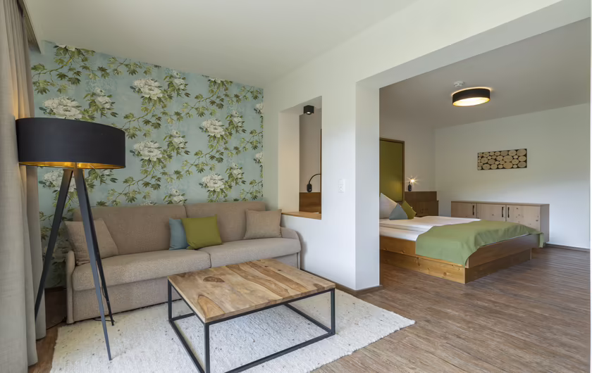 Sitzecke mit Couch und kleinem Tisch - blau / grüne Blumen Tapete im Hintergrund